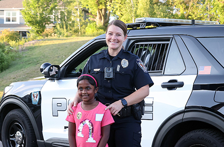 A Plymouth Police Officer standing in front of a squad car with a young resident